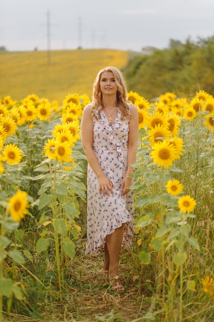Piękna kobieta pozuje w polu uprawnym ze słonecznikiem w słoneczny letni dzień