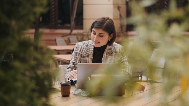 Piękna kobieta przedsiębiorca rozmawiająca z kolegami przez wideorozmowę na laptopie omawiająca nowy projekt podczas przerwy na kawę w kawiarni na świeżym powietrzu