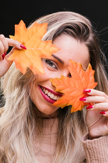 Bezpłatne zdjęcie piękna kobieta trzyma liście klonu przed jej twarzą