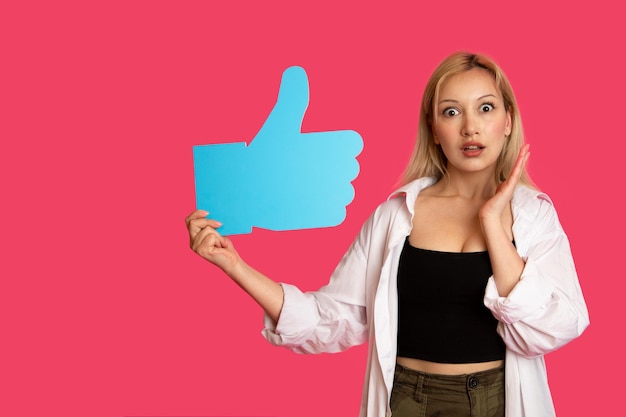 Piękna kobieta trzymająca przycisk "like" na różowym tle