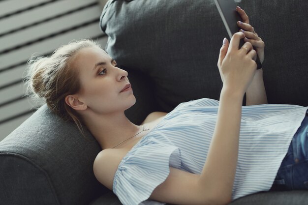 Piękna kobieta używa cyfrową pastylkę, kłama na kanapie