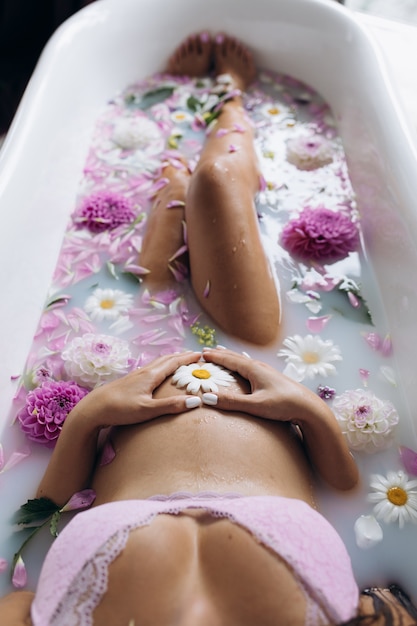 Bezpłatne zdjęcie piękna kobieta w ciąży w różowej bielizny leżącego w wannie pełne różowe kwiaty