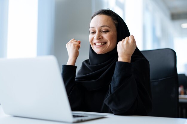 Piękna kobieta w sukience abaya pracuje na swoim komputerze. pracownica w średnim wieku przy pracy w biurze biznesowym w dubaju. pojęcie o kulturach bliskiego wschodu i stylu życia