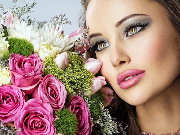 Piękna kobieta z bukietem świeżych kwiatów spting na twarzy. Ładna dziewczyna z makijażem mody