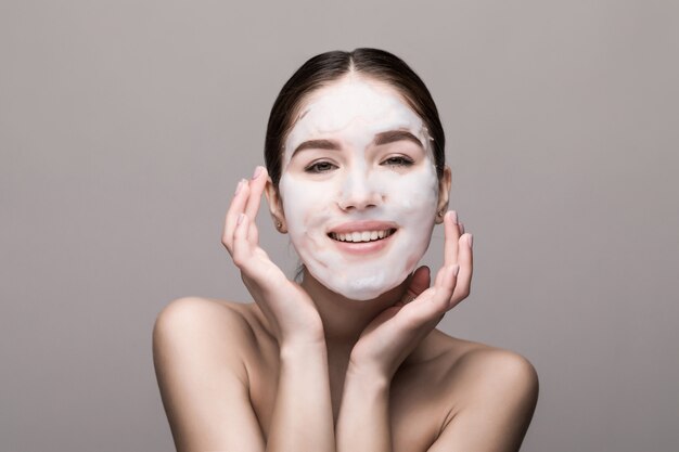 Piękna kobieta z twarzową maską na biel ścianie. Kosmetyki, pielęgnacja skóry.