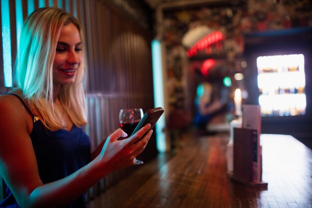 Piękna kobieta za pomocą telefonu komórkowego mając czerwone wino przy ladzie