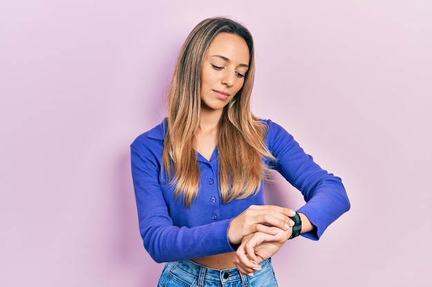 Bezpłatne zdjęcie piękna latynoska kobieta ubrana w swobodną niebieską koszulę sprawdzająca czas na zegarku na rękę, zrelaksowana i pewna siebie