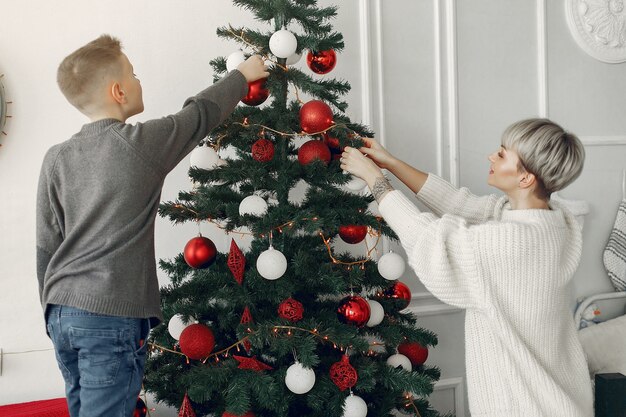 Piękna Mama W Białym Swetrze. Rodzina W Ozdób Choinkowych. Mały Chłopiec W Pokoju