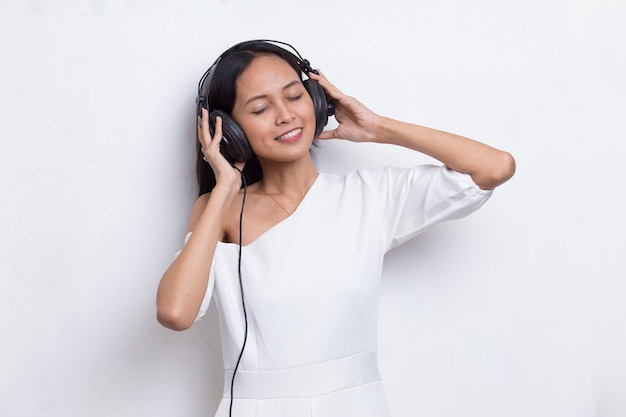 Piękna młoda azjatycka kobieta słucha muzyki na białym tle