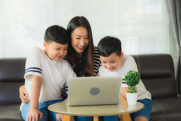 Piękna młoda azjatykcia kobiety mama z jej dwa synami używa laptop na kanapie