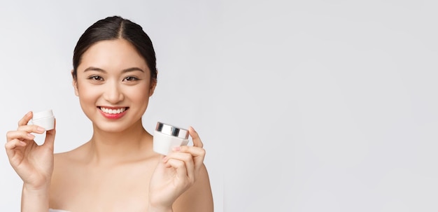 Piękna młoda kobieta na białym tle trzyma kosmetyczny krem do twarzy azjatycki