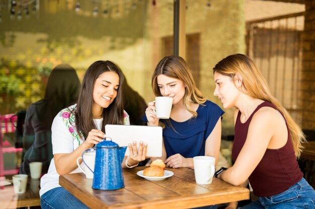 Piękna młoda kobieta pokazuje przyjaciołom coś interesującego na swoim cyfrowym tablecie, siedząc w restauracji