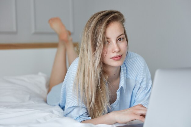 Piękna młoda kobieta relaksuje w łóżku z laptopem