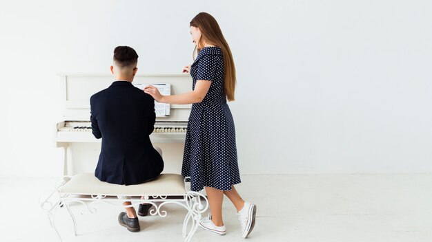 Piękna młoda kobieta stoi blisko mężczyzna bawić się pianino