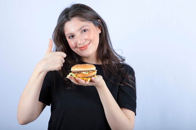 piękna młoda kobieta trzyma pysznego burgera wołowego i daje kciuki do góry.
