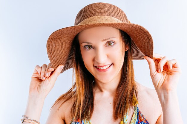 Piękna młoda kobieta ubrana w letnią sukienkę, kapelusz na białym tle z miejsca na kopię, ściskając kapelusz na plaży. koncepcja letniej mody na plaży