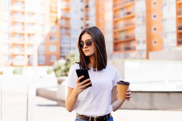 Piękna młoda kobieta używa jej mądrze telefon z uśmiechem podczas gdy chodzący outdoors