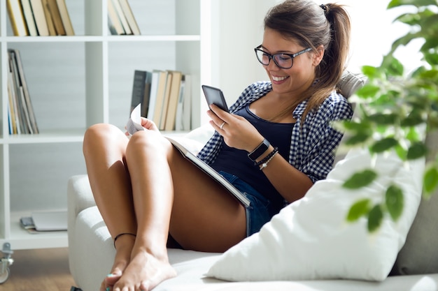 Bezpłatne zdjęcie piękna młoda kobieta używa jej telefon komórkowego w domu.