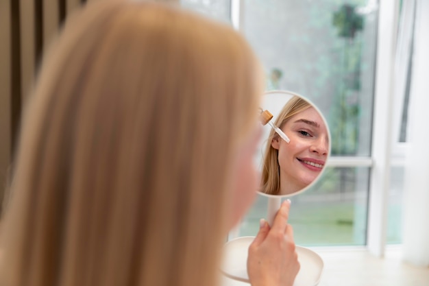 Bezpłatne zdjęcie piękna młoda kobieta używa olejku do pielęgnacji twarzy