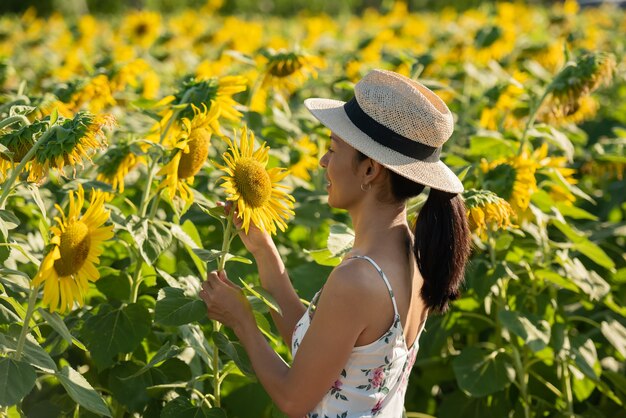 Piękna młoda kobieta w polu słoneczników w białej sukni. podróż na koncepcji weekendu. portret autentycznej kobiety w słomkowym kapeluszu. Na zewnątrz na polu słonecznika.