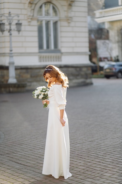 Piękna młoda kobieta w ślubnej sukni pozuje na ulicie w mieście