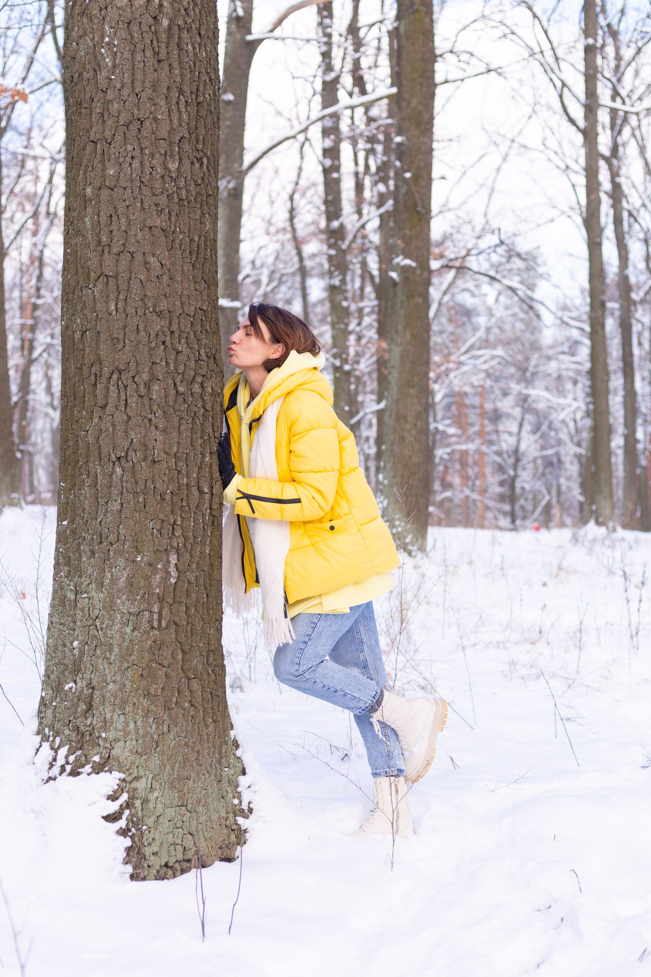 Piękna młoda kobieta w zimowym lesie okazuje czułe uczucia do natury, pokazuje swoją miłość do drzewa