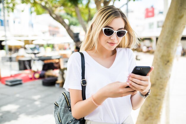 Piękna młoda kobieta za pomocą inteligentnego telefonu na zewnątrz na ulicy słoneczne lato