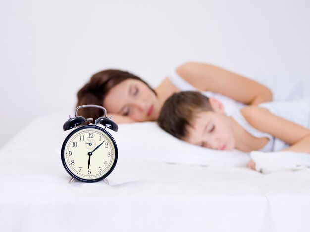 Piękna młoda matka i jej syn w wieku przedszkolnym śpi z budzikiem