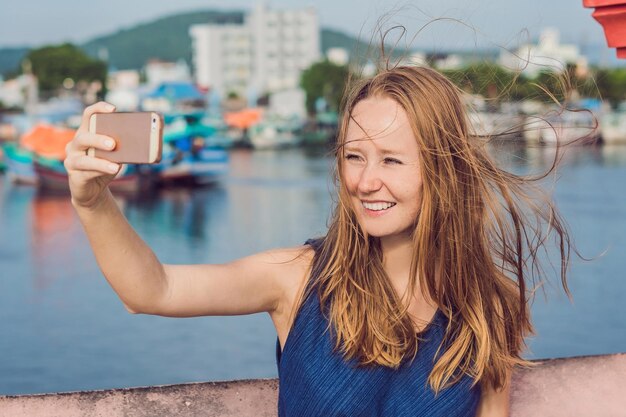 Piękna młoda wesoła kobieta robi selfie na tle morza i wietnamskich łodzi.