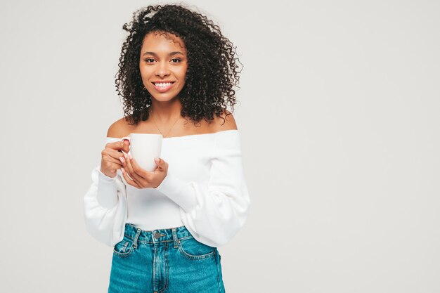 Piękna murzynka z afro lokami fryzurę. Uśmiechnięta modelka w swetrze i modnych dżinsach