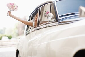 Piękna panna młoda siedzi z ślubnym bukietem w retro samochodzie i zabawę