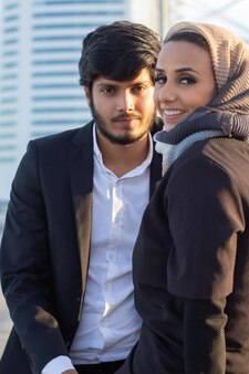 Piękna para arabska spędzająca razem czas. kobieta z zakrytą głową i jasnym makijażem i mężczyzna w garniturze siedzi patrząc na kamery. koncepcja miłości, uczucia