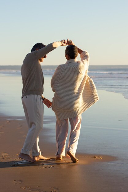 Piękna para starszych tańczy nad brzegiem morza, spędzając razem czas o zachodzie słońca. Szczęśliwy człowiek kręcenie krótkowłosą damą pod pachą. Wakacje, romans, koncepcja emerytury