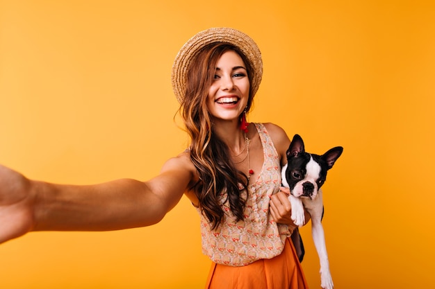 Piękna Rudowłosa Dziewczyna Z Buldogiem Francuskim Dokonywanie Selfie. Zainspirowana Modelka Pozuje Na Pomarańczowo Z Czarnym Szczeniakiem.