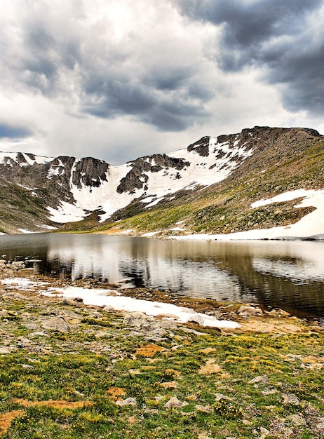 Bezpłatne zdjęcie piękna sceneria jeziora otoczonego wysokimi skalistymi ośnieżonymi górami pod zachmurzonym niebem