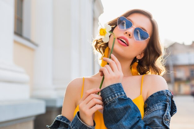 Piękna seksowna stylowa kobieta w żółtej stylowej sukience na sobie dżinsową kurtkę, modny strój, trend w modzie wiosna lato, słoneczne, niebieskie okulary przeciwsłoneczne, moda uliczna, styl hipster, modne akcesoria