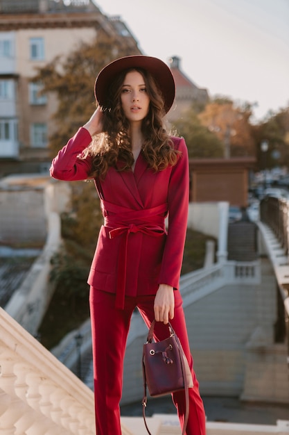Piękna stylowa kobieta w fioletowym garniturze spaceru ulicą miasta, trend w modzie wiosna lato jesień sezon w kapeluszu, trzymając torebkę