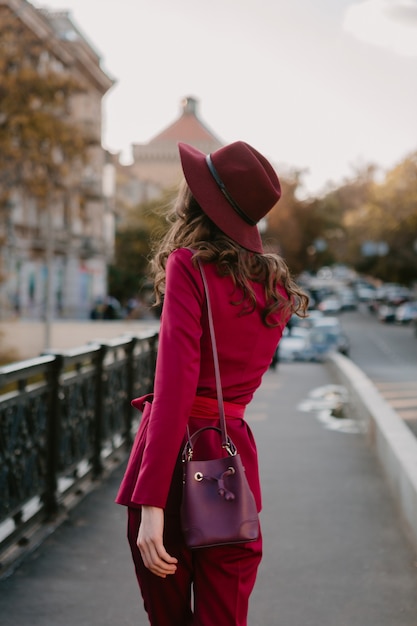 Piękna stylowa kobieta w fioletowym garniturze spaceru ulicą miasta, trend w modzie wiosna lato jesień sezon w kapeluszu, trzymając torebkę