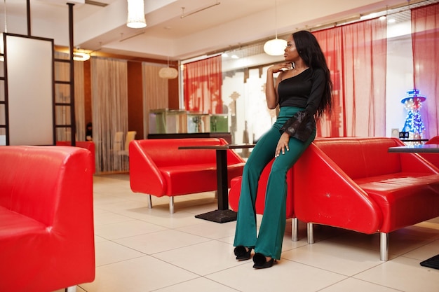 Piękna szczupła afroamerykańska modelka nosi czarną bluzkę i zielone spodnie z długimi nogawkami pozowane w chińskiej kawiarni