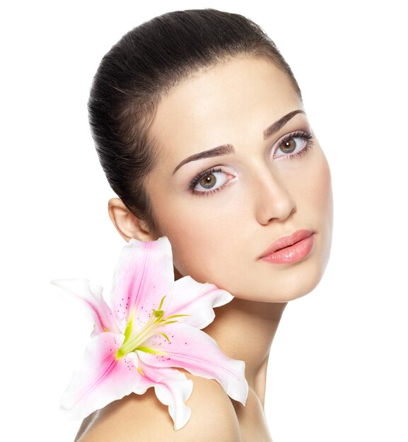 Piękna twarz młodej kobiety z kwiatem. Koncepcja zabiegów kosmetycznych. Portret na białej ścianie