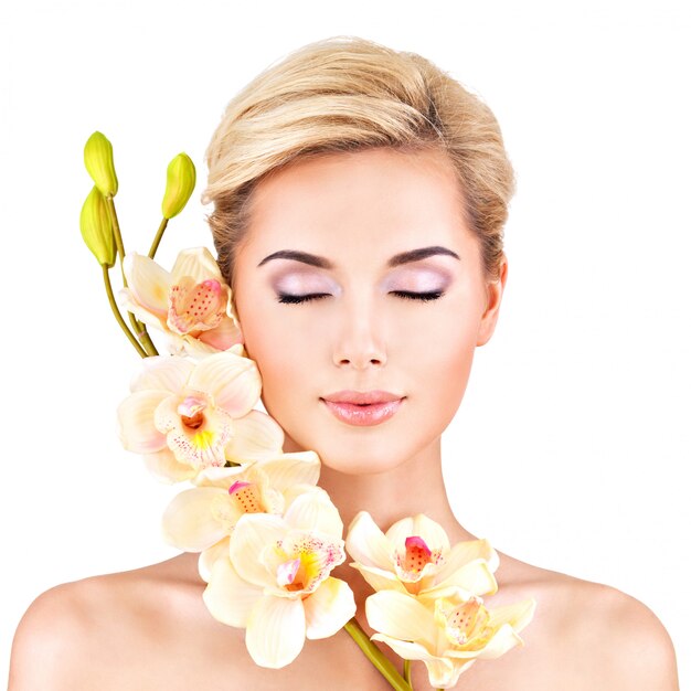 Piękna twarz młodej ładnej kobiety ze zdrową skórą i różowe kwiaty na ciele - na białym tle
