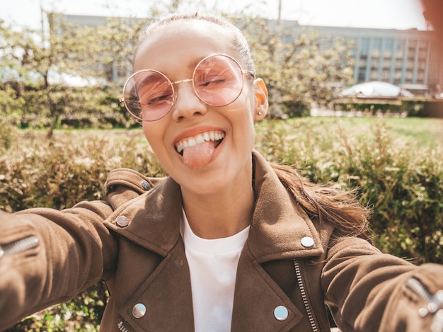 Piękna Uśmiechnięta Dziewczyna W Lato Hipster Kurtka I Dżinsy Model Selfie Biorąc Na Smartfonie I Pokazując Język