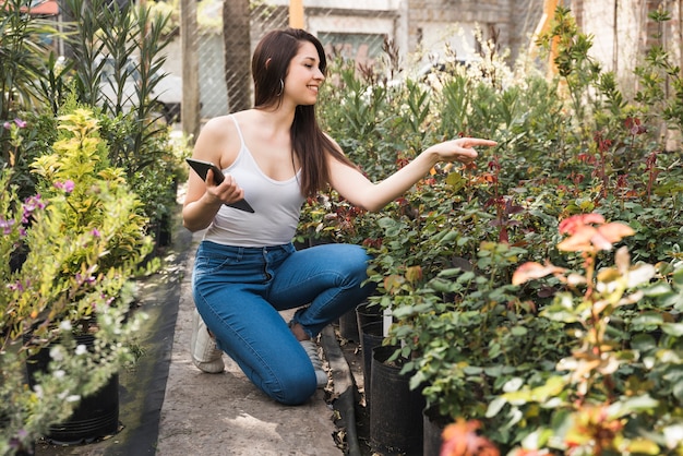 Piękna żeńska ogrodniczka trzyma cyfrową pastylkę w ręce wskazuje palec w kierunku rośliien
