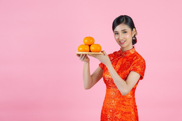 Piękne azjatyckie kobiety szczęśliwy uśmiech i trzymając świeże pomarańcze w chińskim nowym roku na różowym tle.
