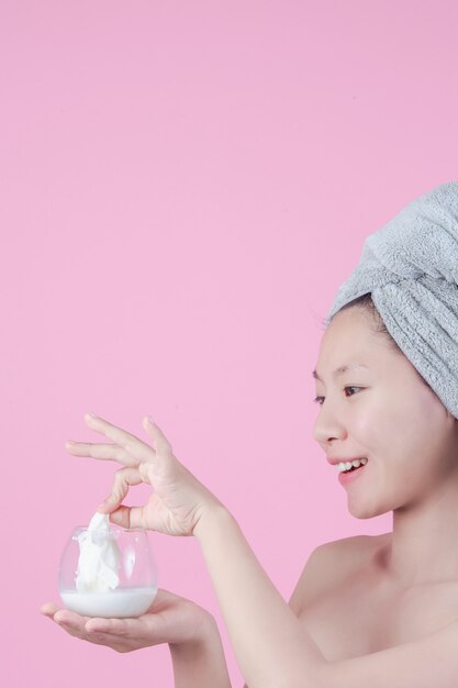 Piękne Azjatyckie kobiety używają twarzy maski twarz na prześcieradle na różowym tle.