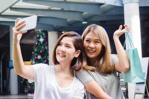 Piękne azjatykcie dziewczyny trzyma torba na zakupy, używać mądrze telefon selfie i ono uśmiecha się