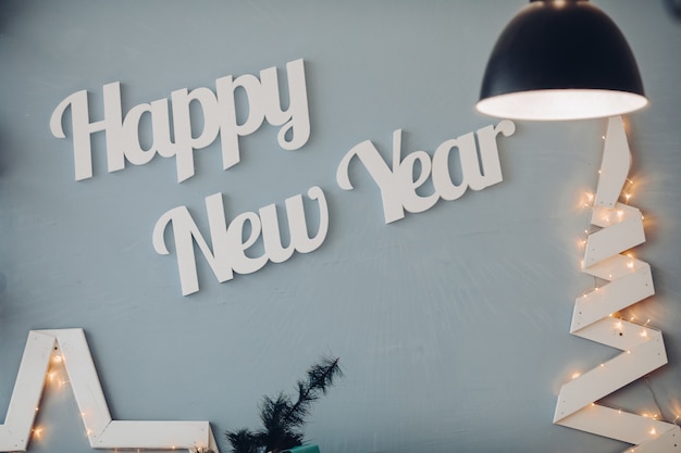 Piękne białe litery szczęśliwego nowego roku na niebieskiej ścianie w nowoczesnym studio dekoracji. Przytulne świąteczne wnętrze w przytulnej designerskiej sali otoczonej światłem ozdobnej lampy vintage