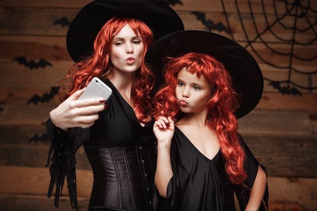 Piękne Caucasian Matka I Córka Z Długimi Czerwonymi Włosami W Kostiumach Czarownic Przy Selfie Premium Zdjęcia