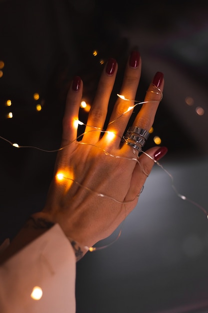 Piękne ciemne zdjęcie kobiecych palców dłoni z dużym srebrnym pierścieniem na kwiatach i świecących światłach