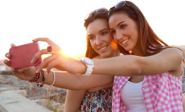 Bezpłatne zdjęcie piękne dziewczyny biorące selfie na dachu o zachodzie słońca.